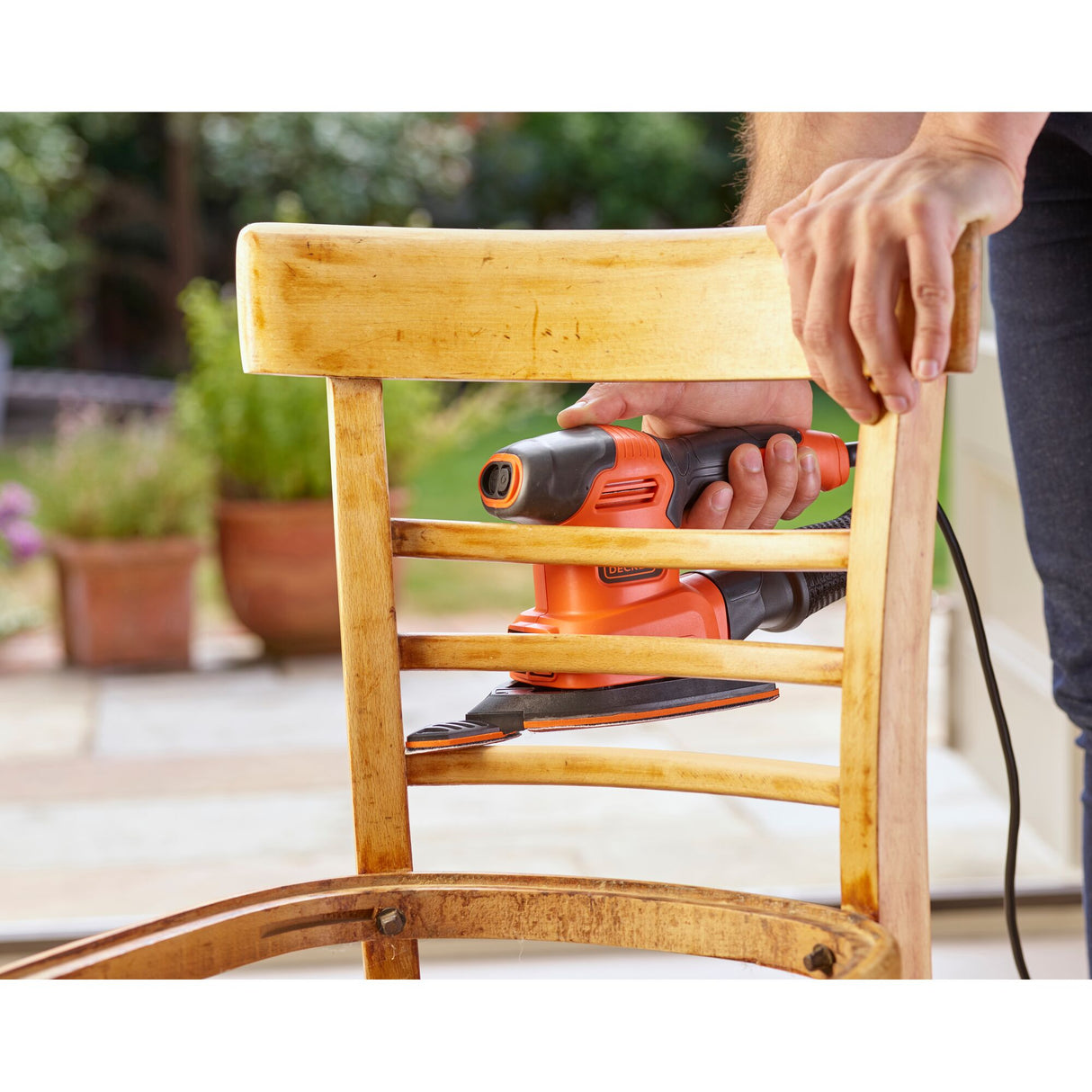 Ponceuse électrique Black+Decker orange en cours d’utilisation sur une chaise en bois