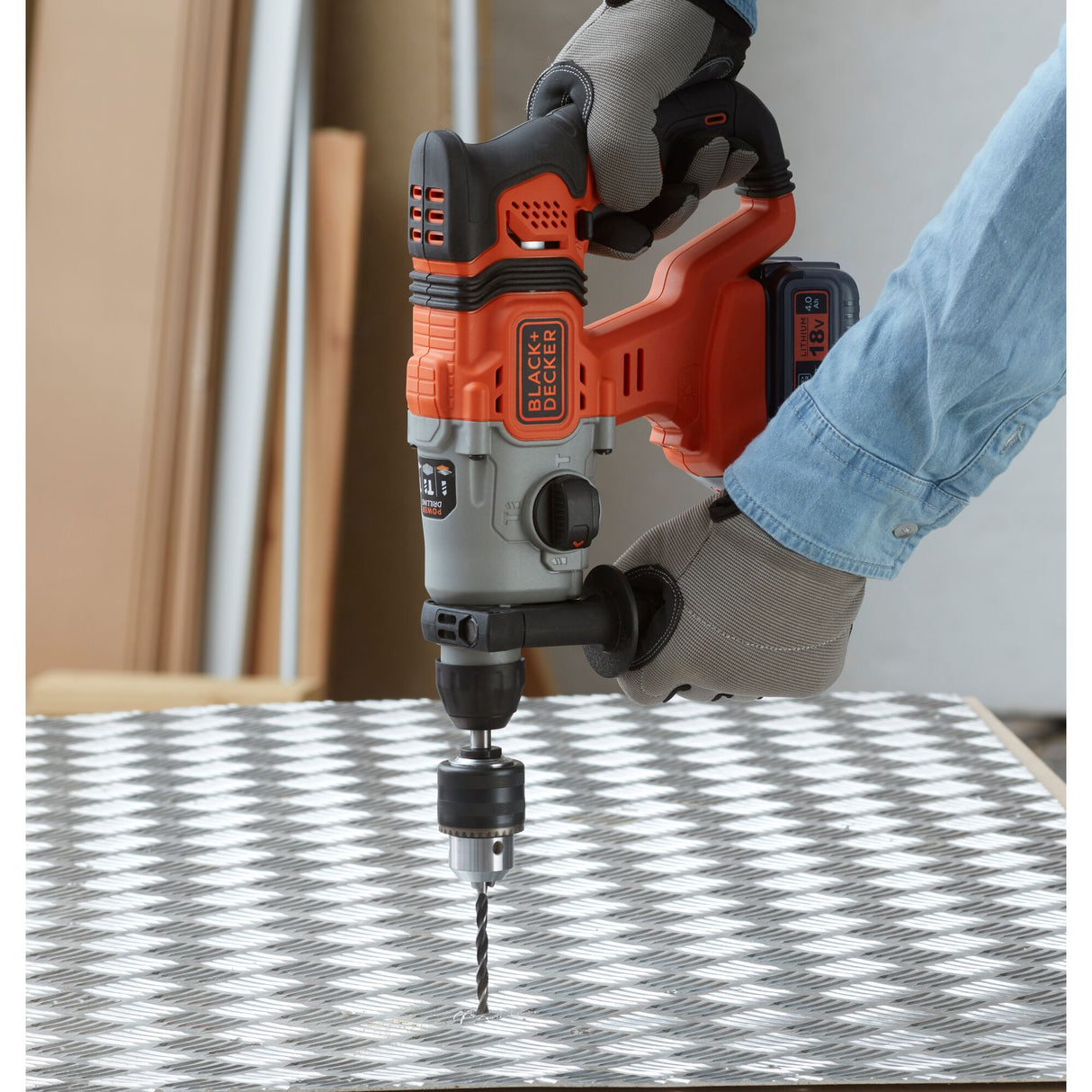 Perceuse BLACK+DECKER, type perforateur, couleur orange et noire, en utilisation sur métal.