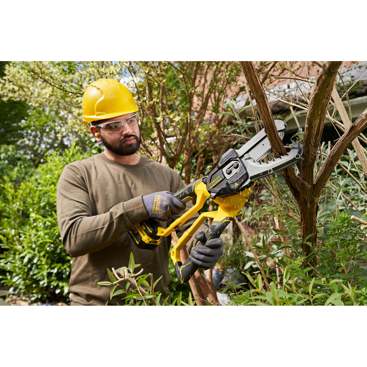 Élagueuse électrique Stanley jaune utilisée pour tailler une branche, outil de jardinage.