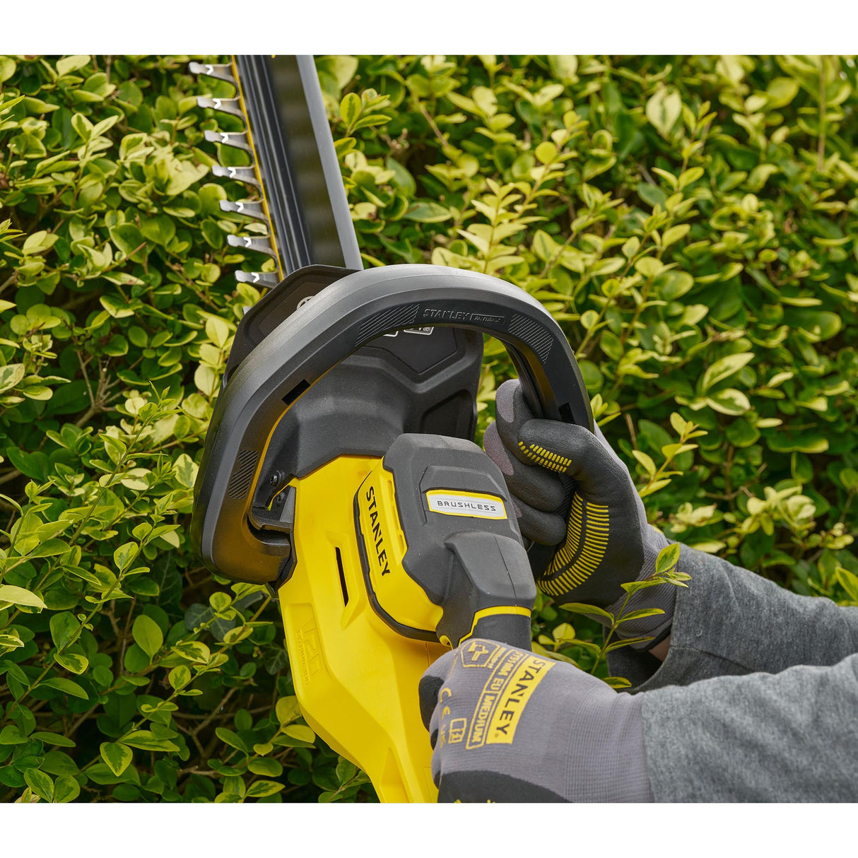 Taille-haie électrique Stanley jaune utilisé en extérieur, marque visible sur l'appareil.
