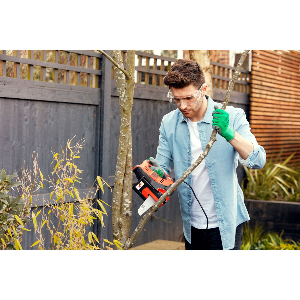 Homme utilisant une tronçonneuse Black+Decker orange et noire pour couper une branche d'arbre