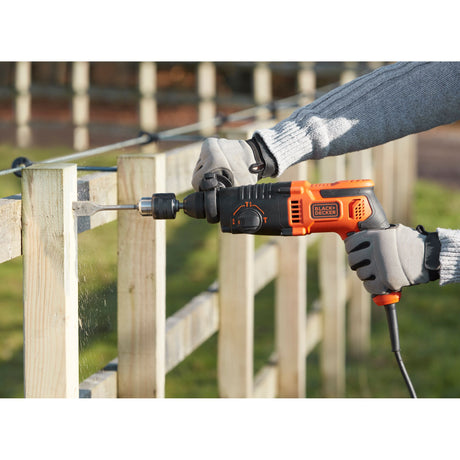 Perceuse BLACK+DECKER, outil électroportatif, couleur noire et orange, en usage sur bois.