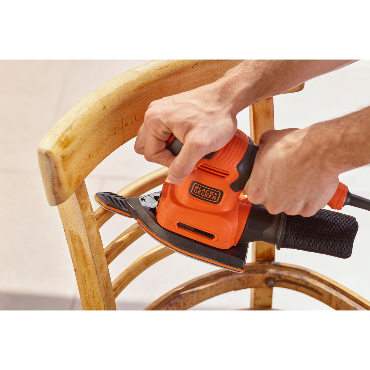 Ponceuse électrique Black+Decker orange en action sur une chaise en bois.