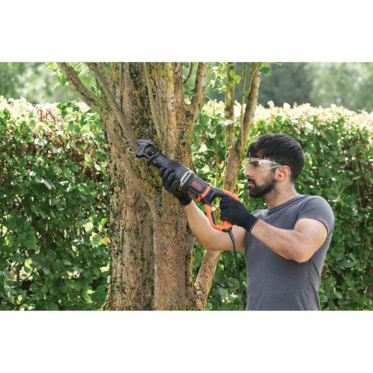 Scie sabre BLACK+DECKER noire et orange pour élagage, utilisée pour couper une branche d'arbre
