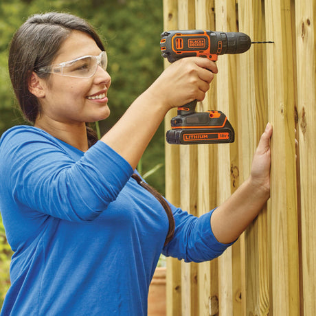 Perceuse visseuse Black+Decker, outil électroportatif noir et orange, en utilisation.