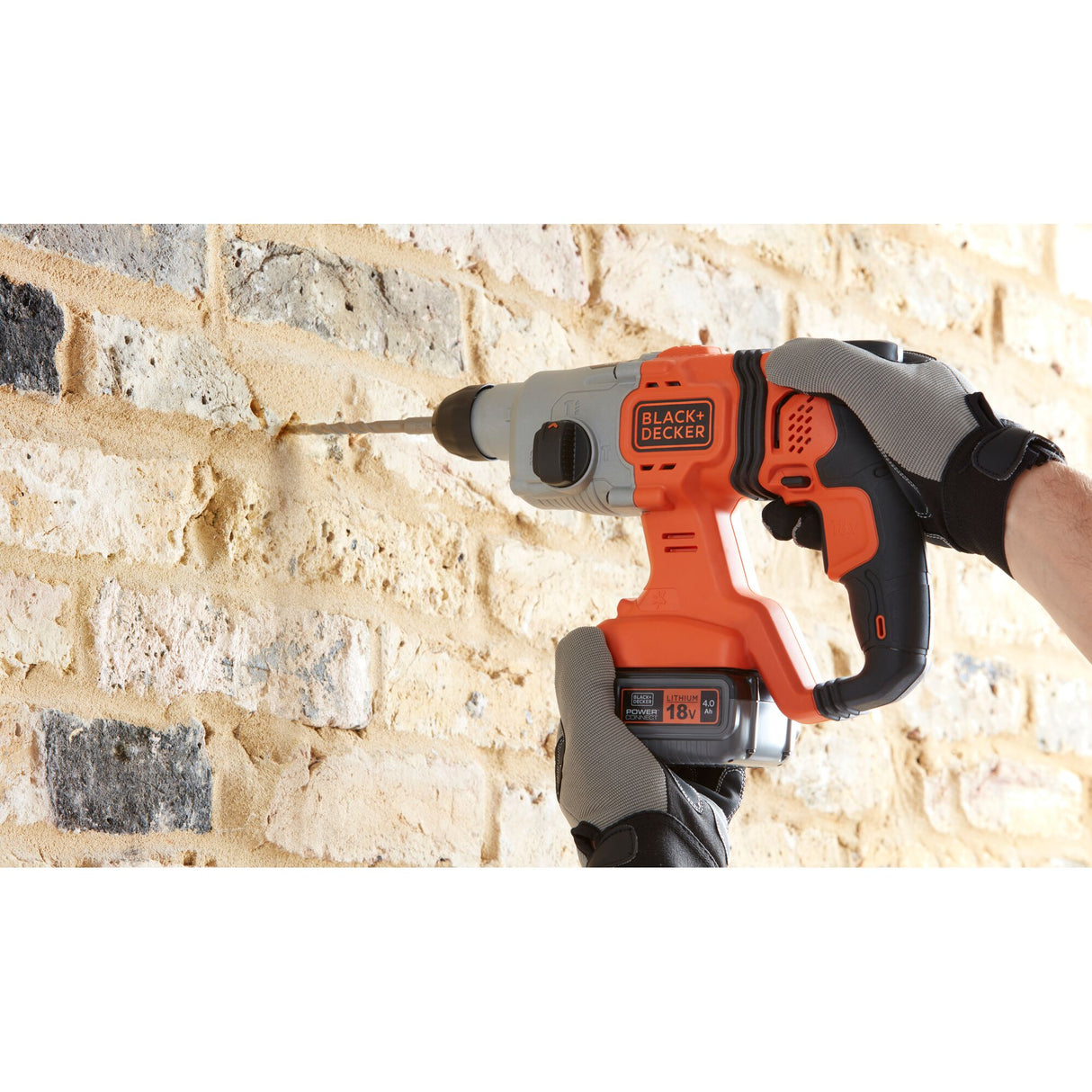 Perceuse-visseuse Black+Decker orange et noire sans fil en action sur mur de briques.