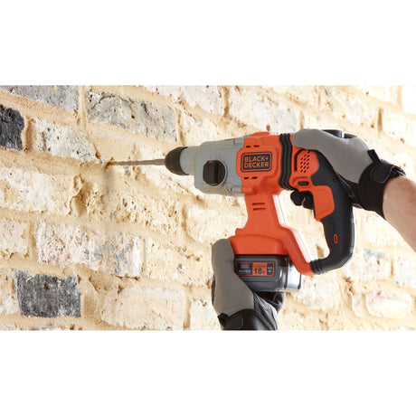 Perceuse-visseuse Black+Decker orange et noire sans fil en action sur mur de briques.