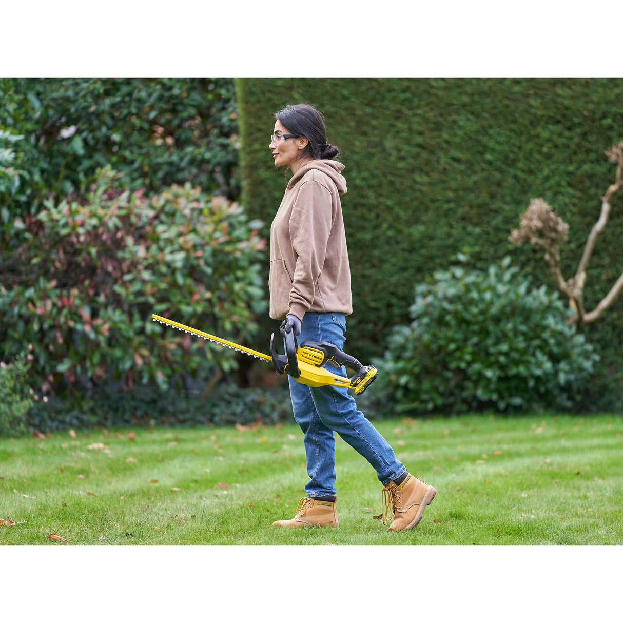 Femme utilisant un taille-haie jaune et noir de marque DeWalt dans un jardin