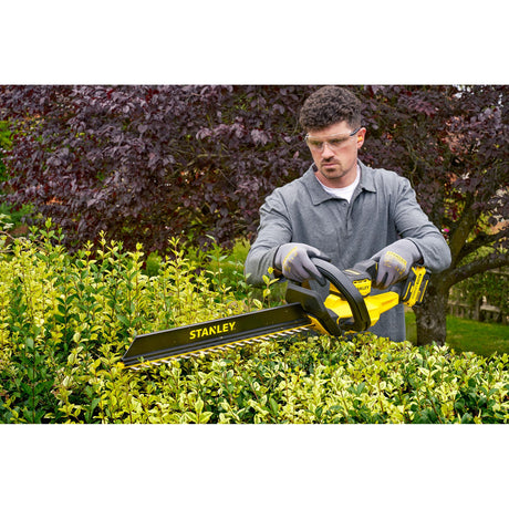 Taille-haie Stanley jaune et noir utilisé pour tailler une haie dans un jardin
