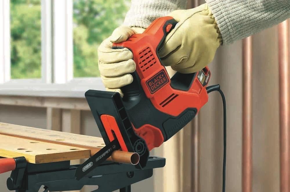 Scie électrique Black+Decker, outil électroportatif rouge et noir, en action sur tube cuivre.