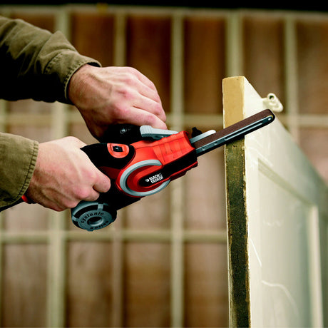 Ponceuse à bande noire et rouge Black+Decker utilisée pour poncer une porte, outil électroportatif
