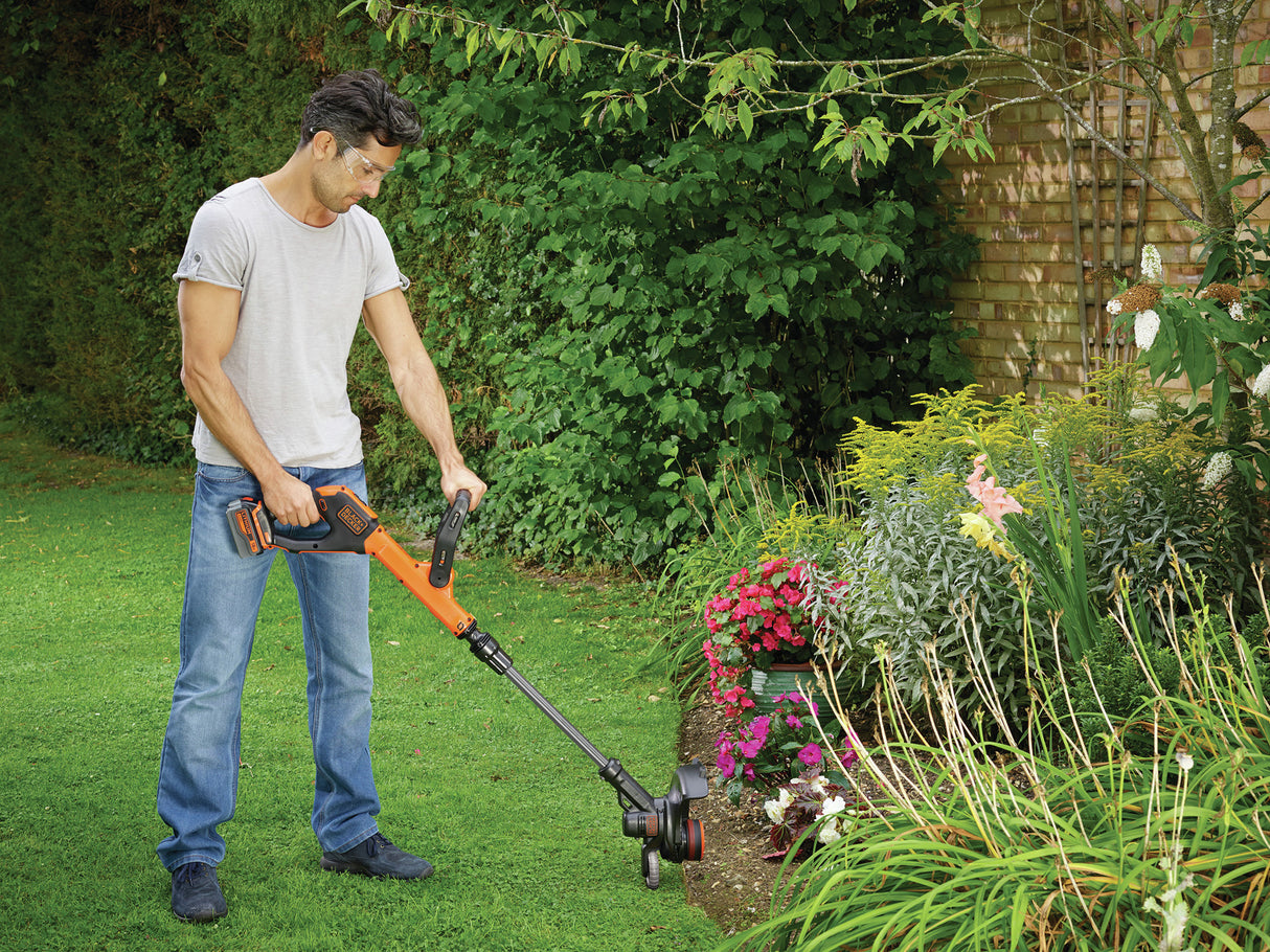 Coupe-bordure Black+Decker orange utilisé pour tailler le gazon dans un jardin fleuri