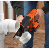 Scie sabre BLACK+DECKER orange découpant un tube PVC blanc, outil électroportatif pour plomberie.