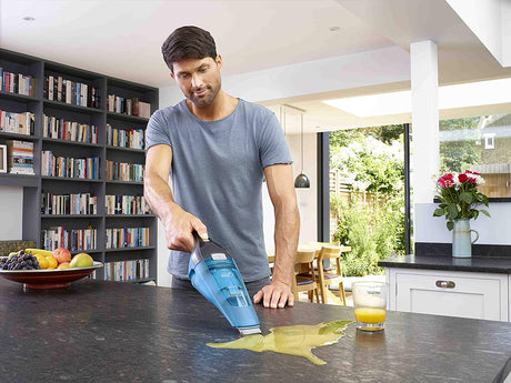 Aspirateur à main Black+Decker, bleu, utilisé pour nettoyer un liquide sur un plan de travail.
